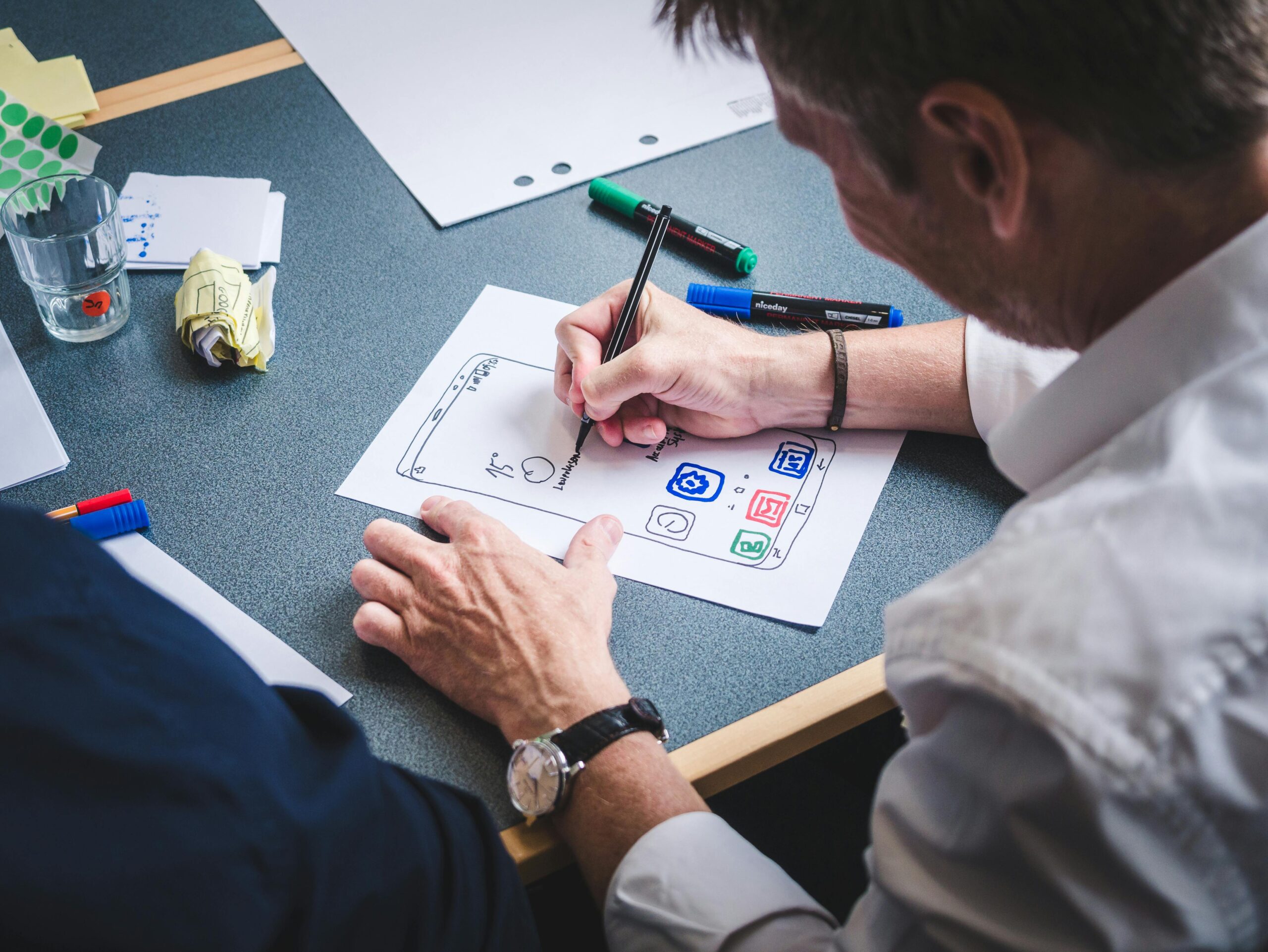 A designer sketches a mobile app prototype on paper at an office desk, focusing on creativity and design.